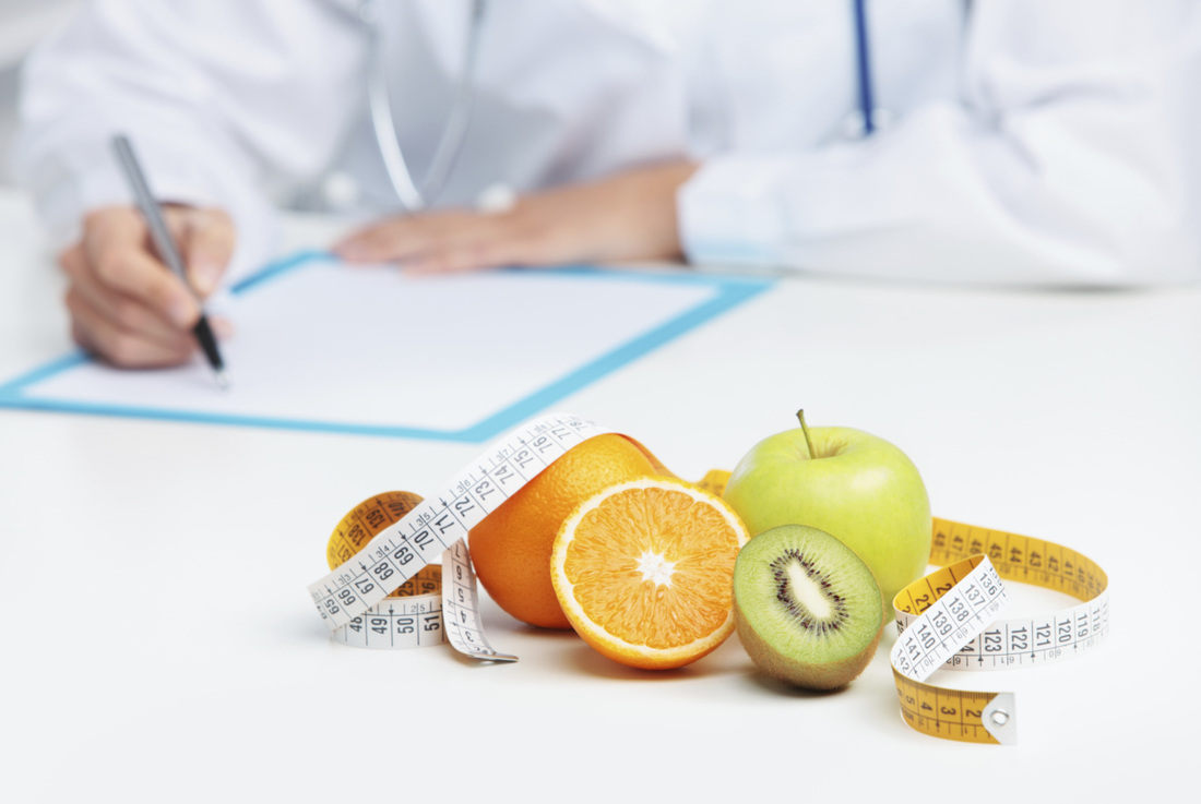"Doktorun önünde masanın üstünde ölçüm bandı ile çevrili portakal, elma ve kivi bulunan bir görsel. Sağlıklı yemek yemek önemi ve ölçümün diyet üzerindeki rolünü temsil eder